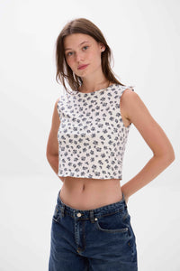 Woman wearing a white floral crop top and blue jeans on a white background.