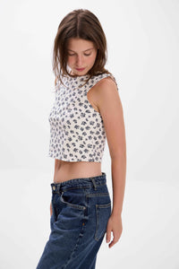 Woman wearing a floral sleeveless top and blue jeans on a white background.