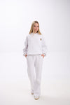 Woman wearing a white hoodie with a small leopard print star and pink accent on the chest, paired with matching white sweatpants and white sneakers, standing against a plain background