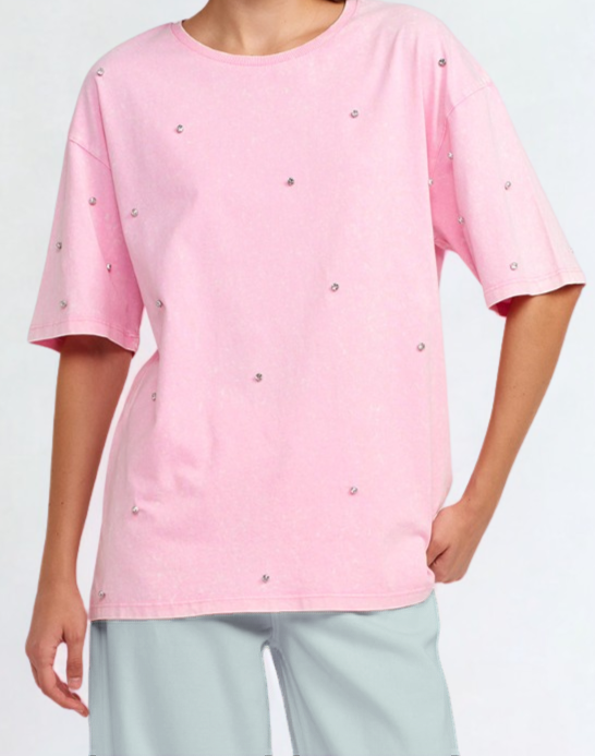 Person wearing a pink t-shirt with decorative buttons on a light gray background.