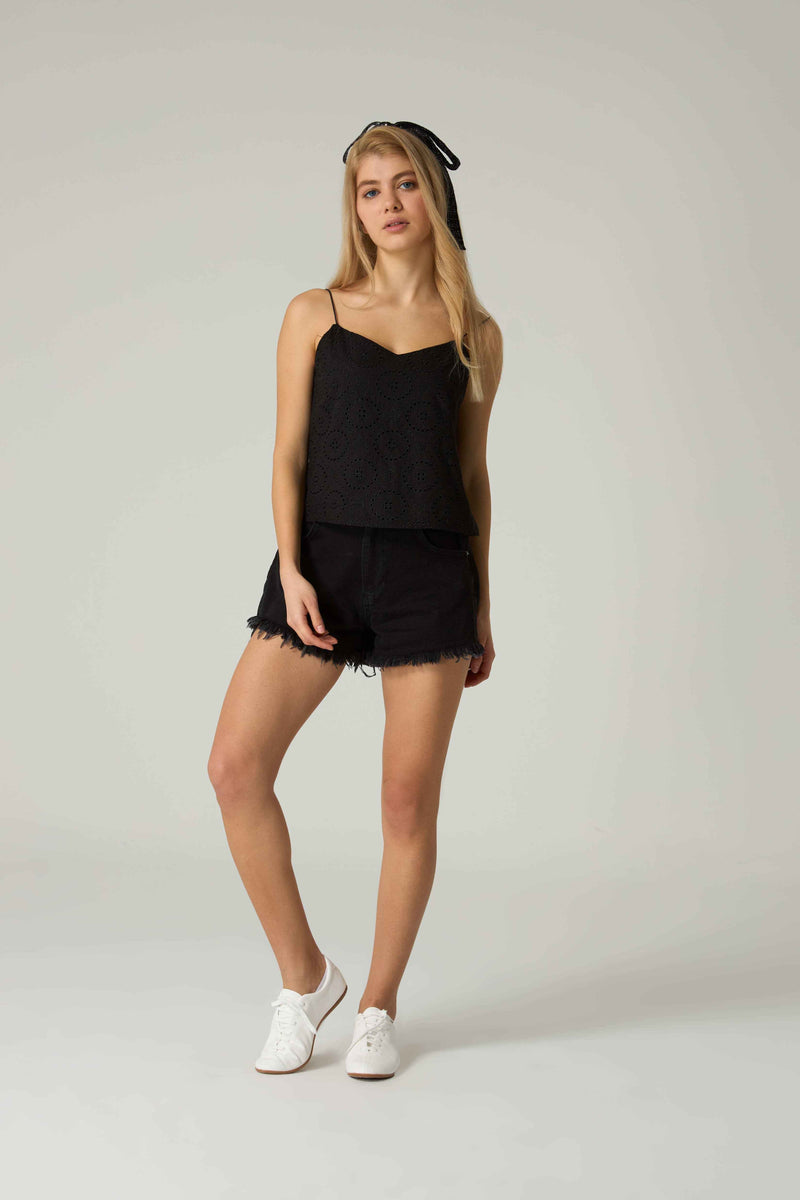 Woman wearing a black sleeveless top and shorts on a plain background.