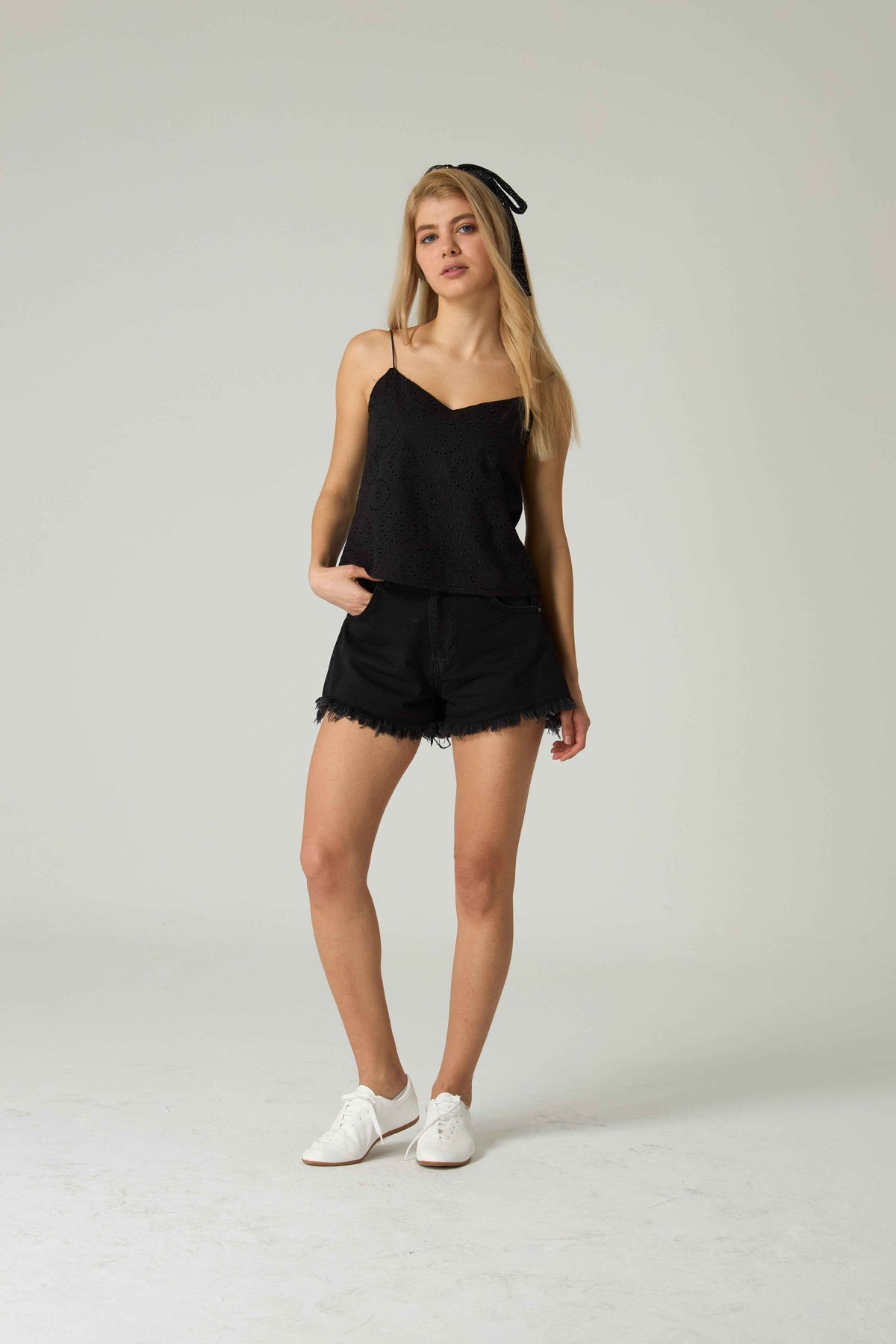 Woman wearing a black outfit with white sneakers on a plain background.