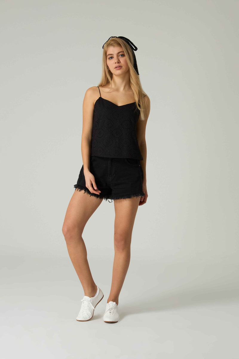 Woman wearing a black sleeveless top and shorts on a plain background.