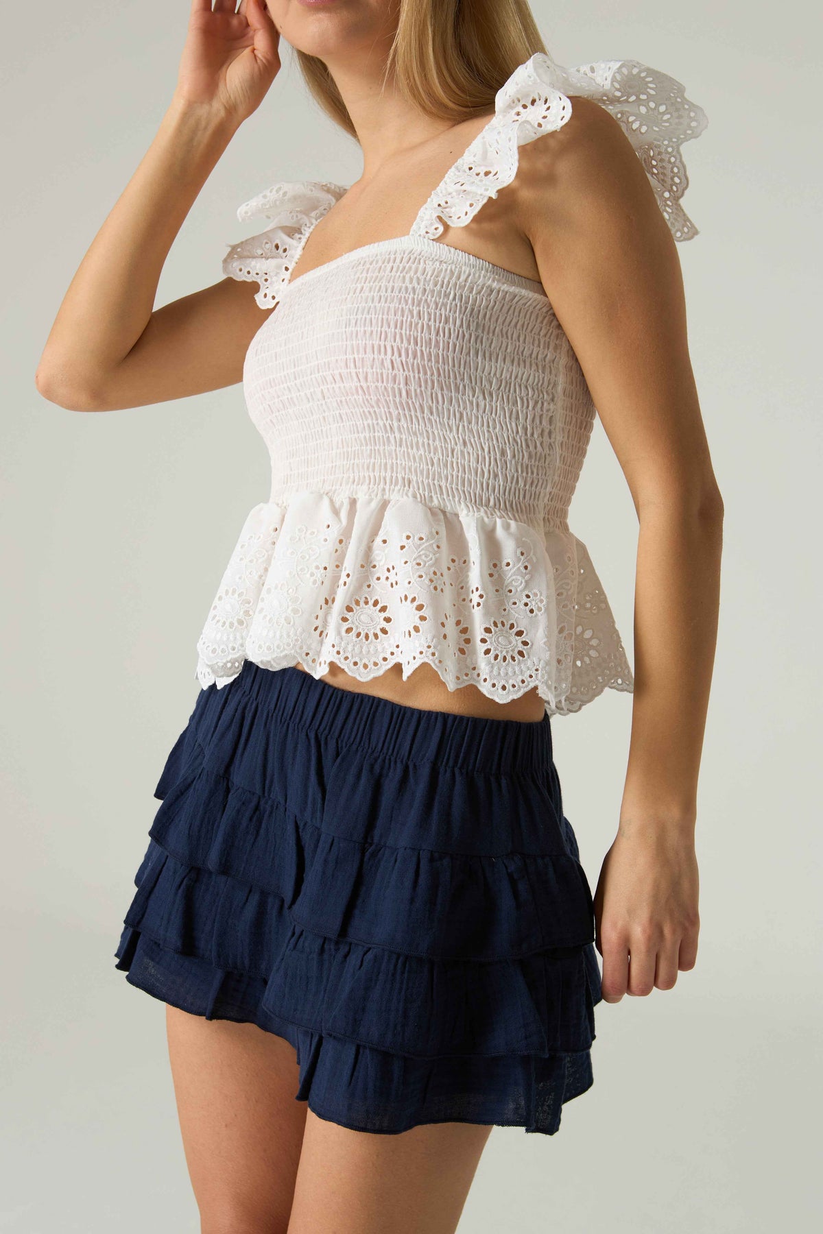 Woman wearing a white top with lace details and a navy blue skirt on a plain background.