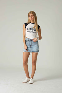 Woman wearing a white and black '1990 England' t-shirt with a denim skirt on a plain background.