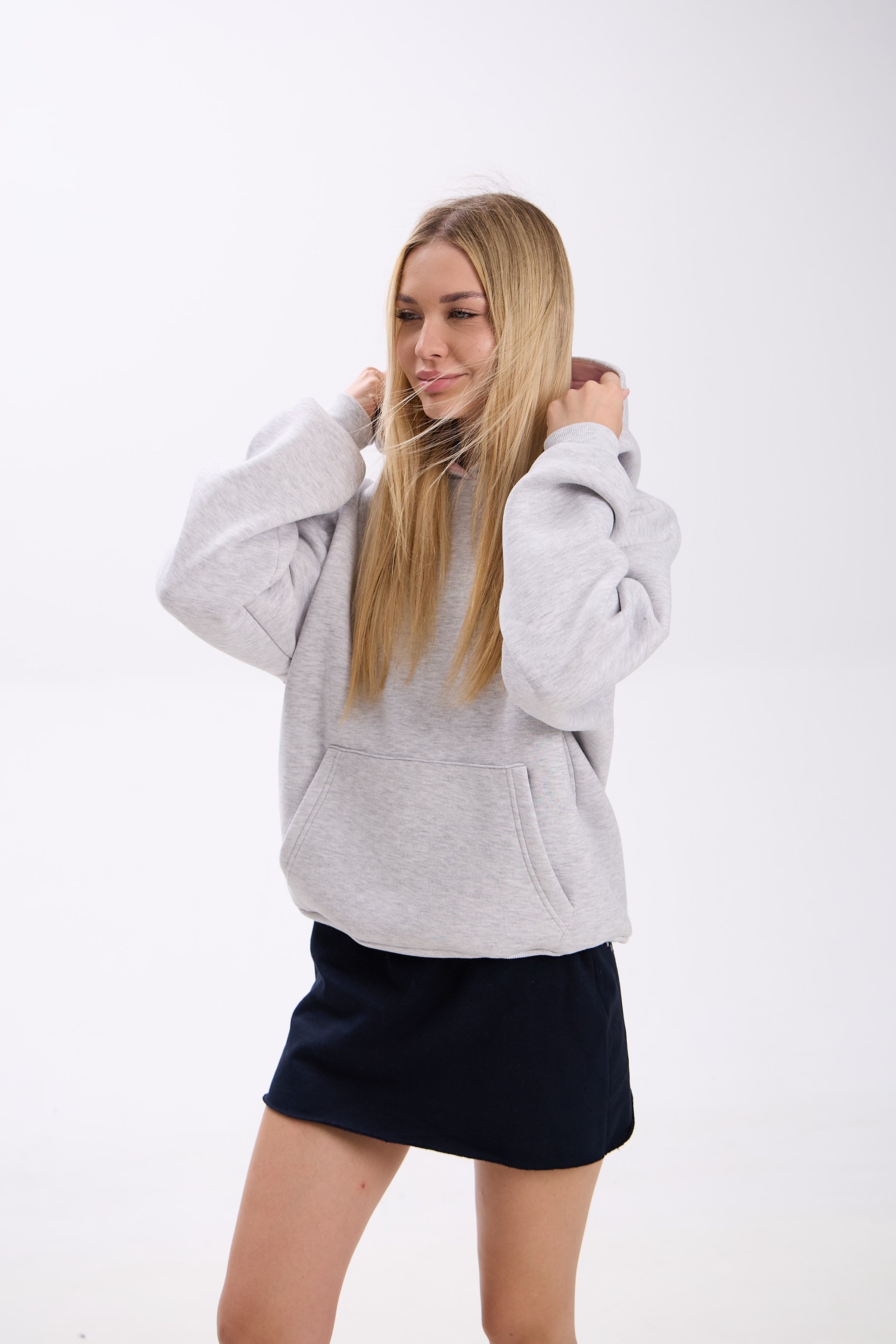 Woman wearing a gray hoodie and navy skirt on a white background