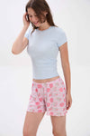 Woman wearing a light blue crop top and pink floral shorts on a white background.