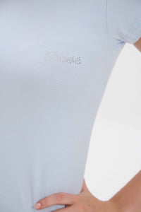 Close-up of a person wearing a light blue shirt with a brand logo on a light gray background.