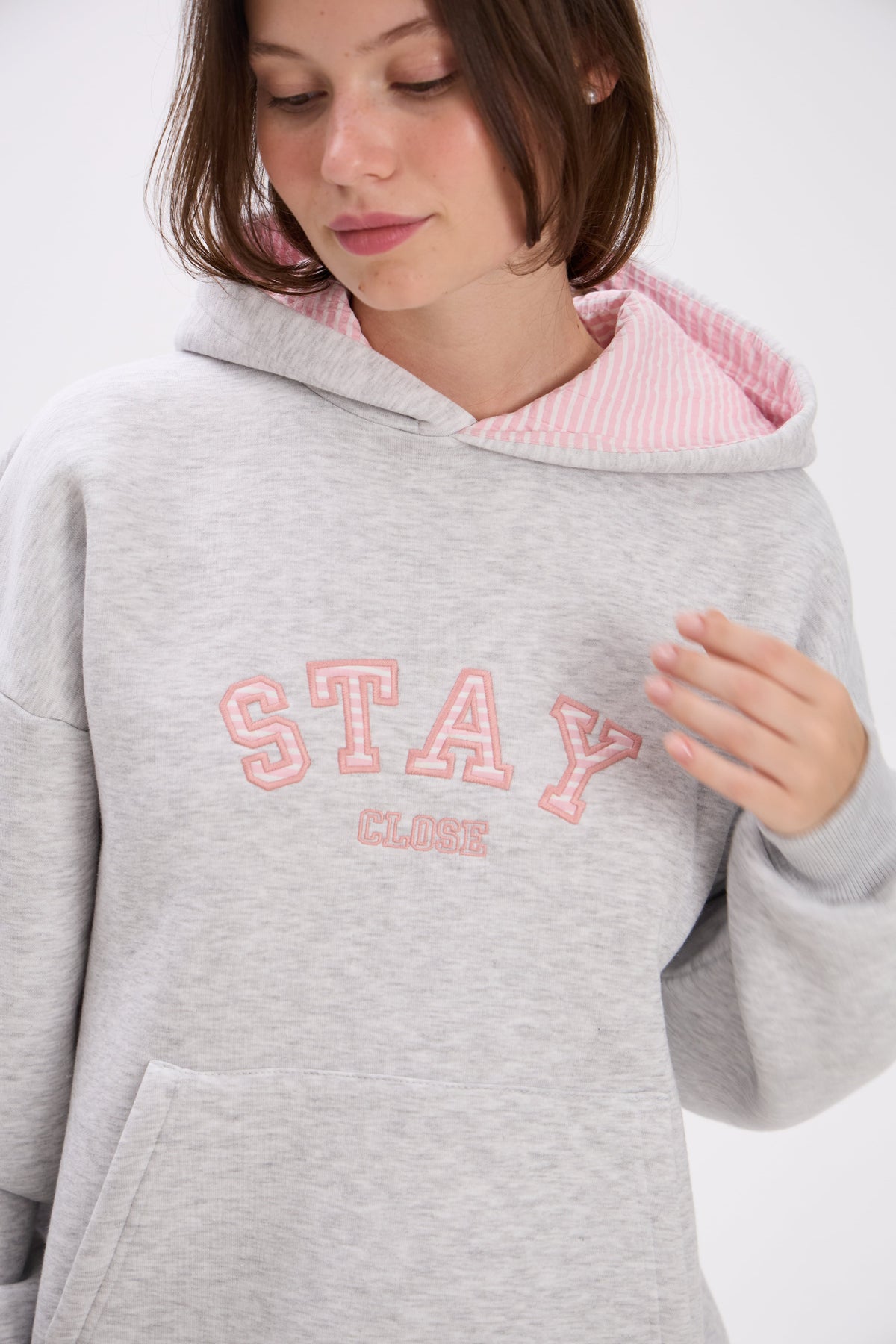 Person wearing a gray hoodie with pink interior and 'Stay Close' text on a white background.