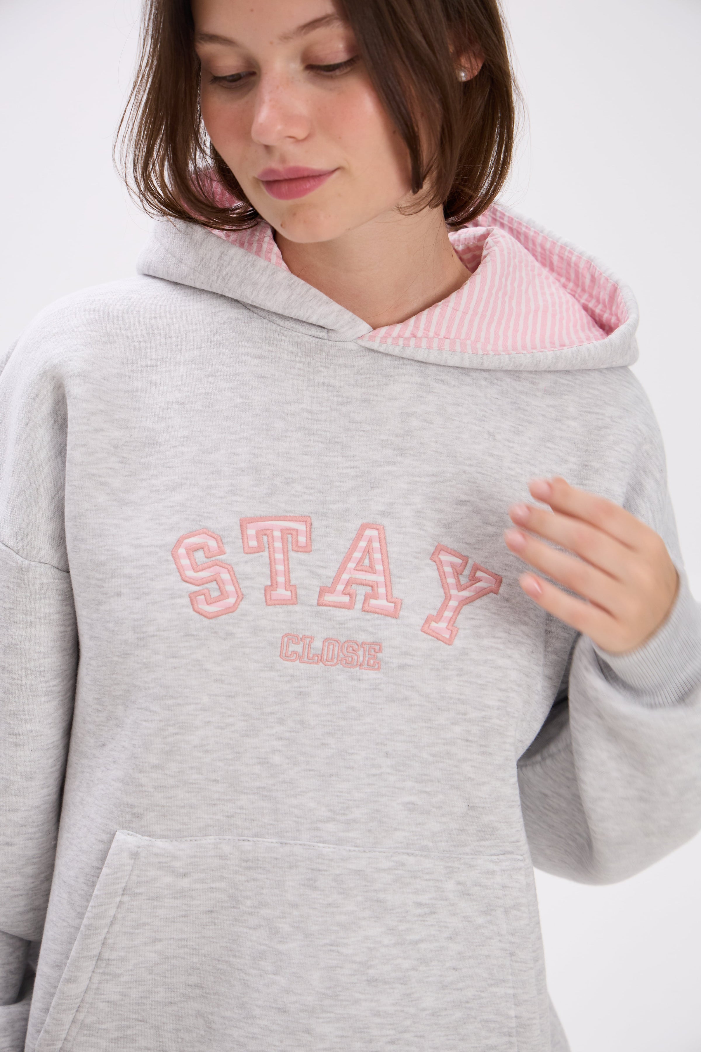 Person wearing a gray hoodie with pink interior and 'Stay Close' text on a white background.