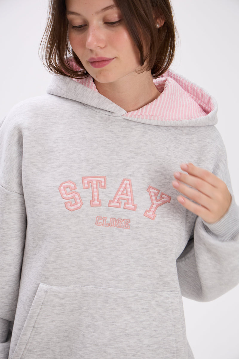 Person wearing a gray hoodie with pink interior and 'Stay Close' text on a white background.