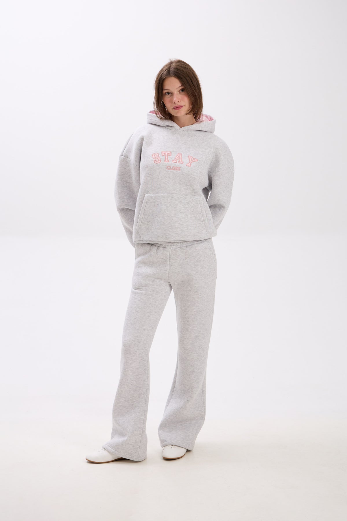 Person wearing a gray hoodie and pants with pink text on a white background.