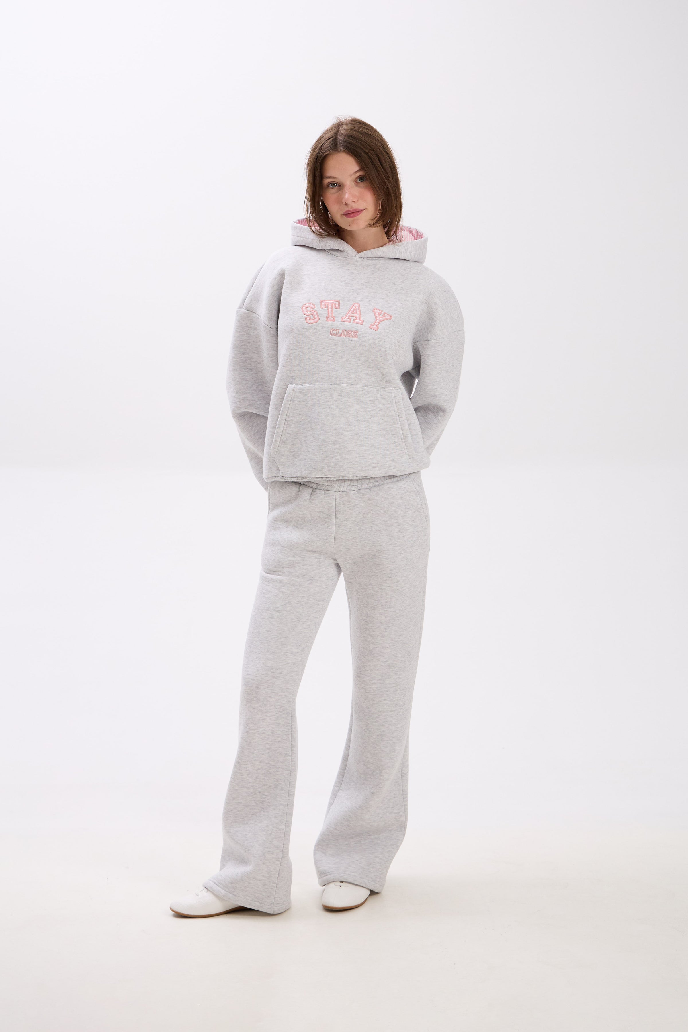 Person wearing a gray hoodie and pants with pink text on a white background.