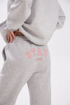 Grey sweatpants with elastic waistband, side pockets, and pink “Stay Close” embroidery on the back.