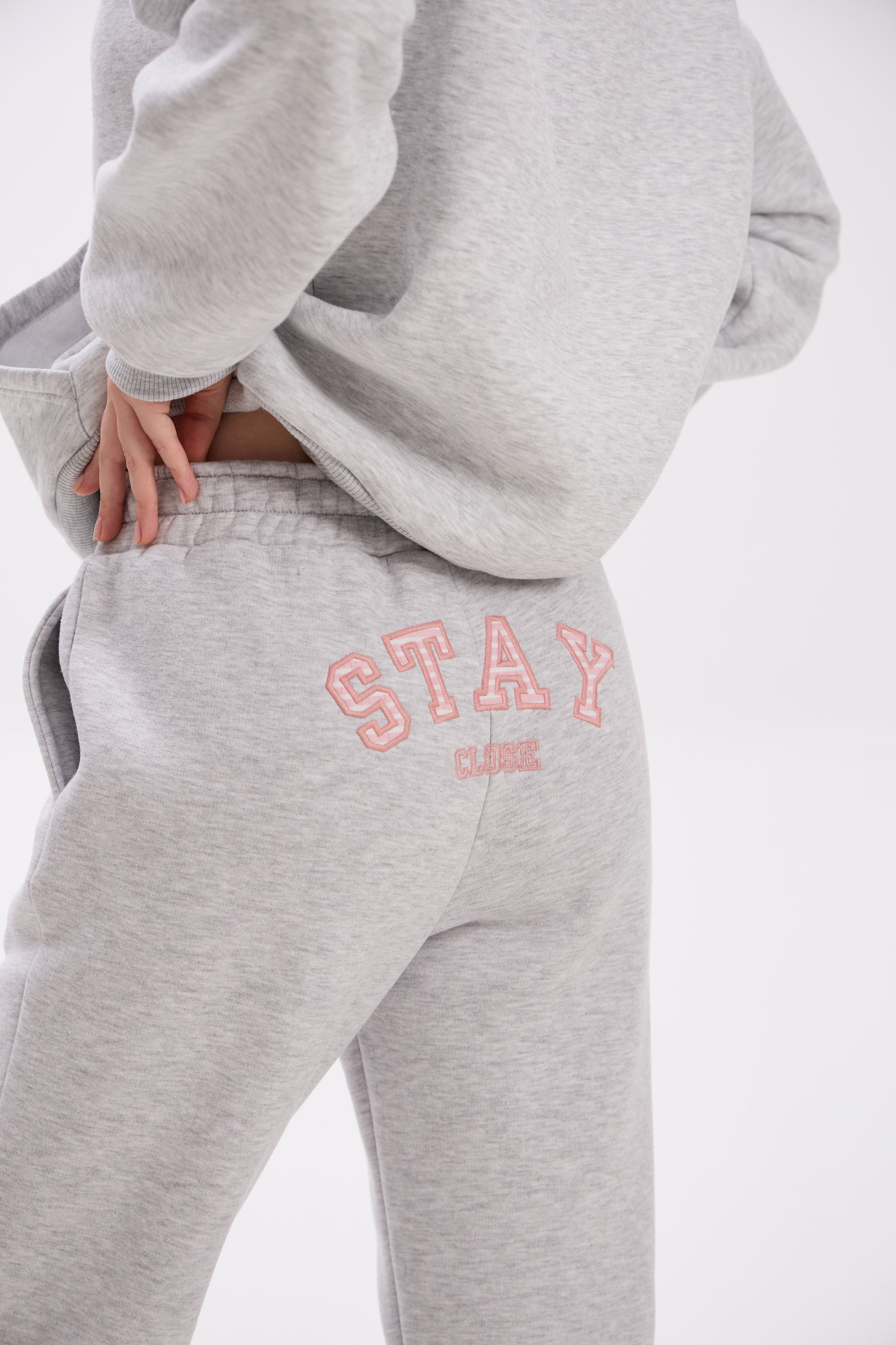 Grey sweatpants with elastic waistband, side pockets, and pink “Stay Close” embroidery on the back.