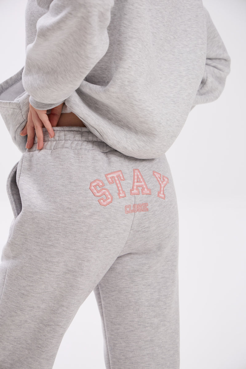 Grey sweatpants with elastic waistband, side pockets, and pink “Stay Close” embroidery on the back.