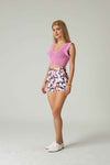 Woman wearing a pink sleeveless top and patterned shorts on a plain background.