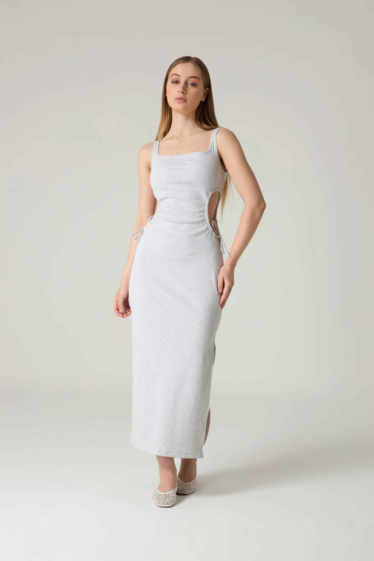 Woman wearing a white dress with cut-out sides on a plain background.