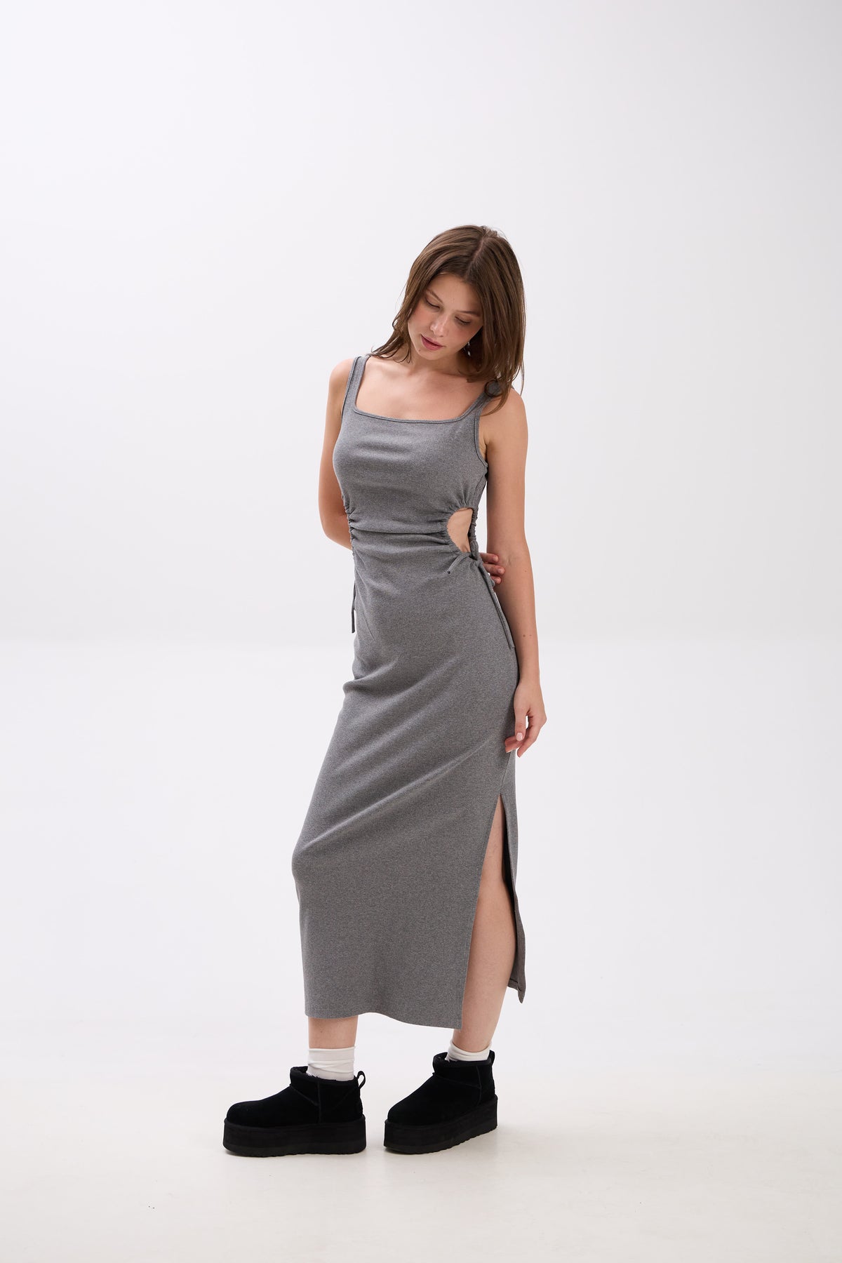 Woman wearing a gray sleeveless dress with a slit on a white background.