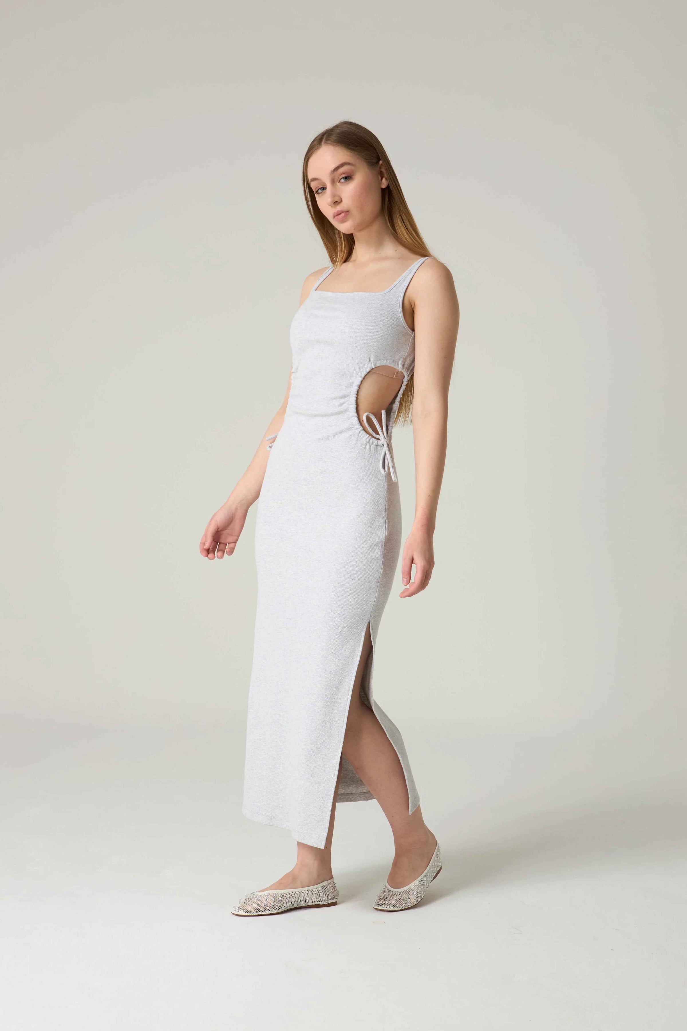 Woman wearing a white dress with cut-out design on a plain background.