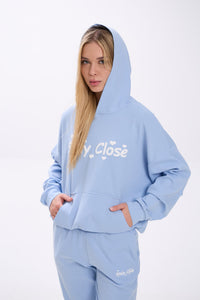 Person wearing a light blue hoodie with white 'Stay Close' text on a white background.