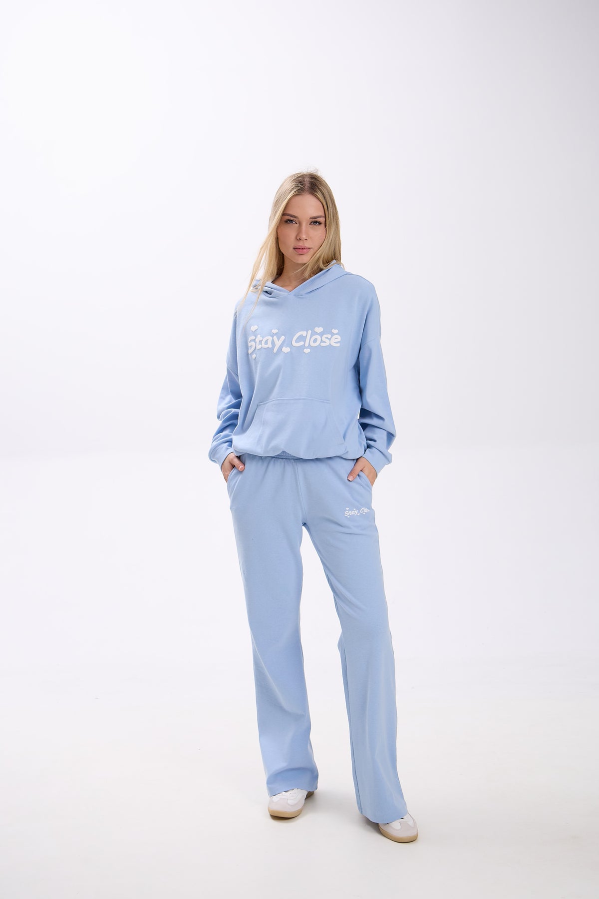Woman wearing a light blue hoodie and sweatpants set on a white background.