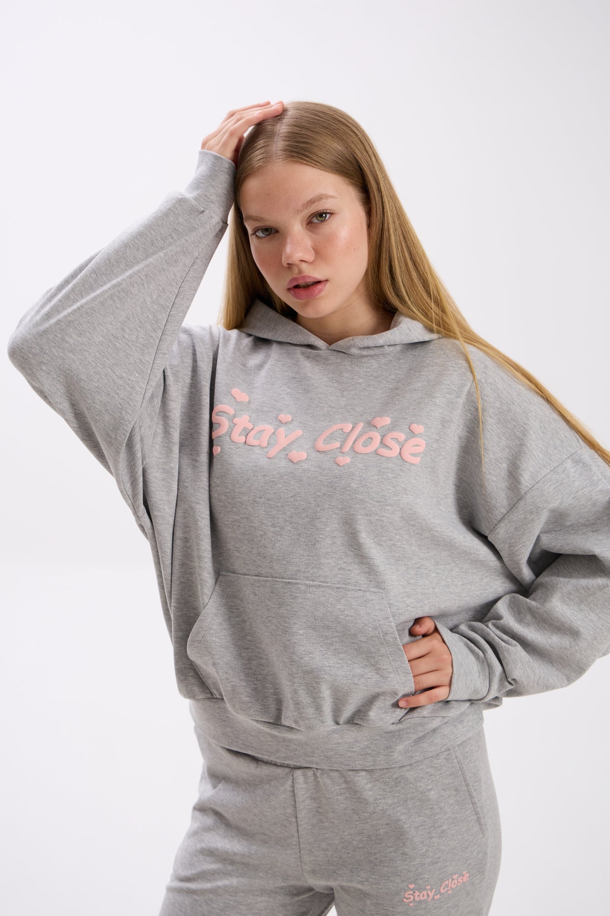 Woman wearing a gray hoodie with pink 'Stay Close' text on a white background.