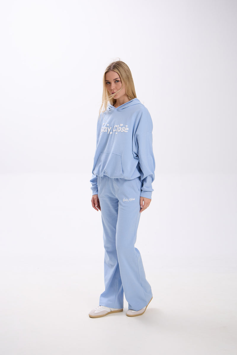 Woman wearing a light blue sweatpants and hoodie on a white background.
