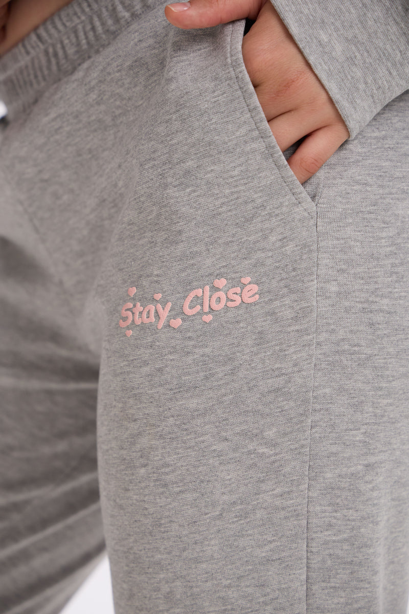 Grey sweatpants with 'Stay Close' text in pink on a white background.