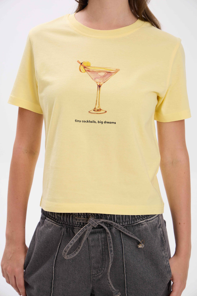Person wearing a yellow t-shirt with a cocktail graphic and text.