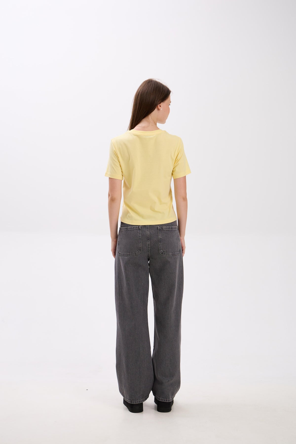 Person wearing a yellow top and gray pants on a white background.
