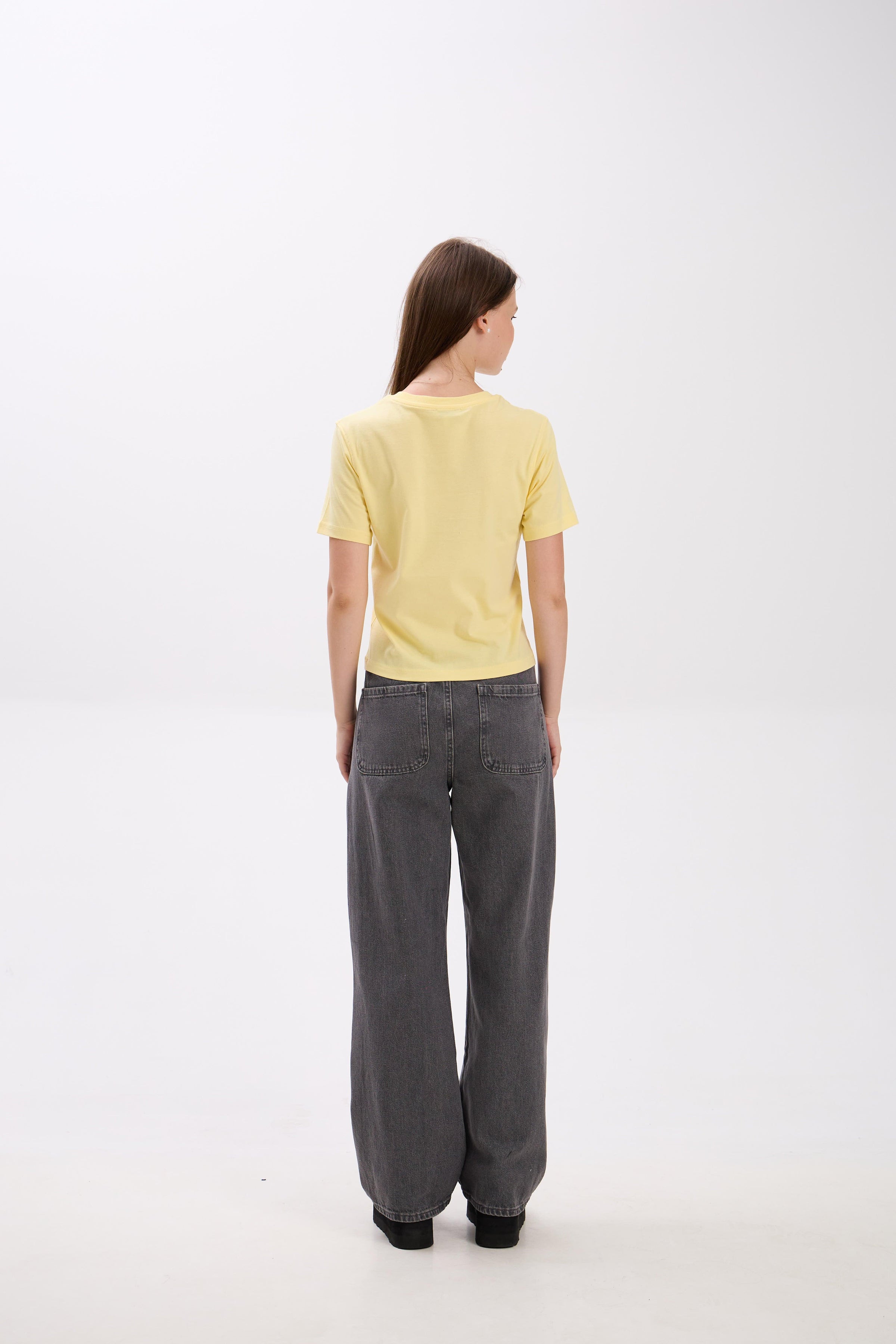 Person wearing a yellow top and gray pants on a white background.