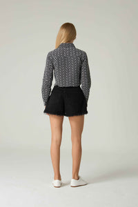 Person wearing a patterned shirt and black shorts on a plain background.