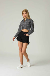 Woman wearing a black and white patterned shirt with black shorts on a light gray background.