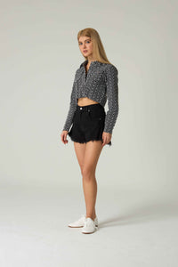 Woman wearing a black and white patterned shirt and black shorts on a light gray background.