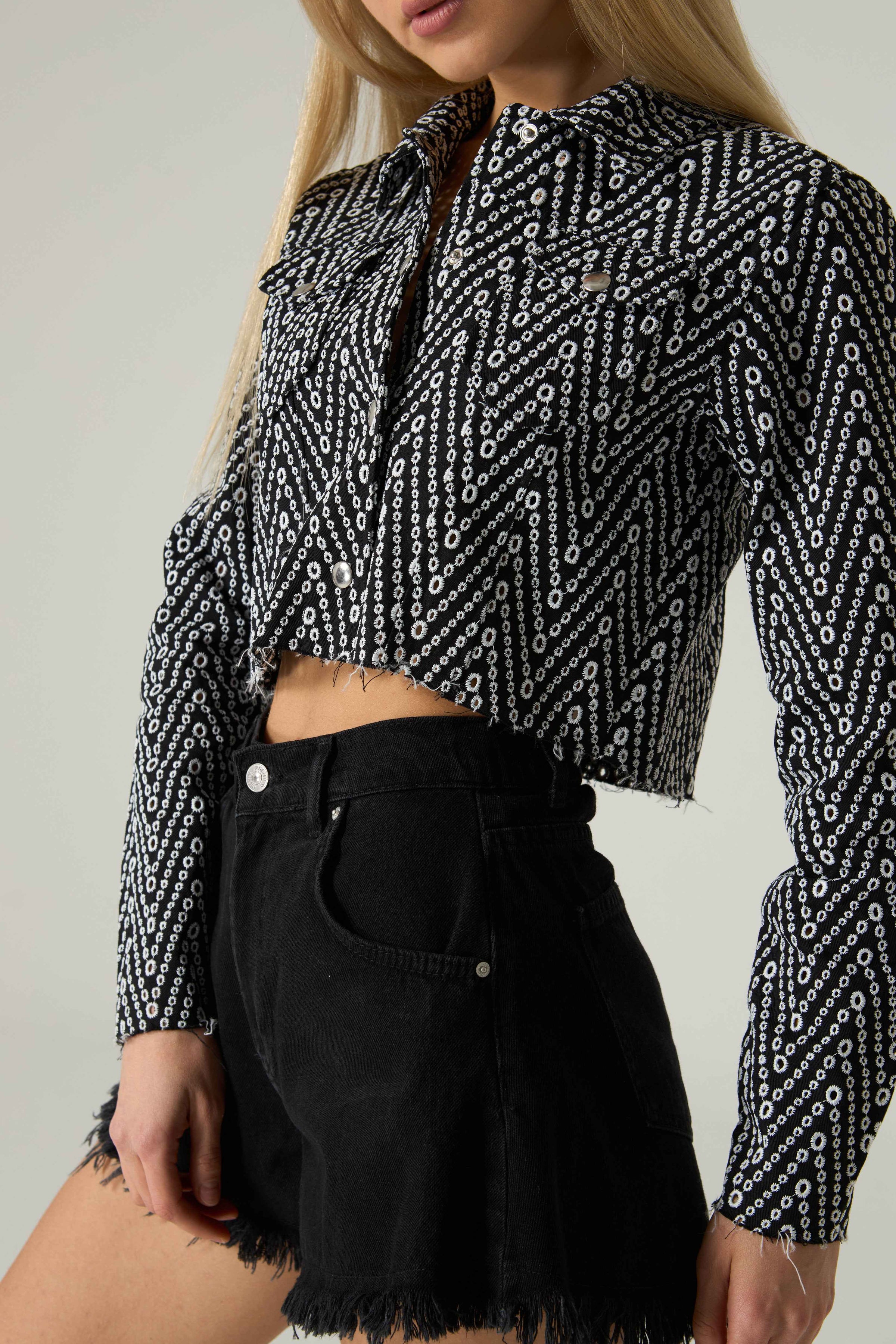 Person wearing a black and white patterned blouse with black shorts on a plain background.