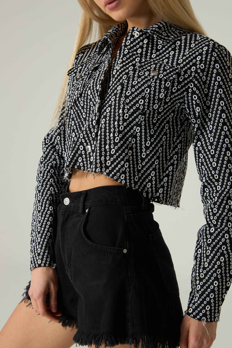 Person wearing a black and white patterned blouse with black shorts on a plain background.