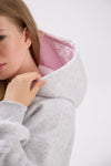 Person wearing a gray hoodie with pink lining on a white background.