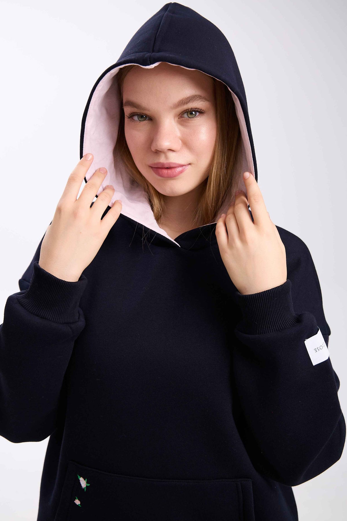 Person wearing a black hoodie with a white patch on a light gray background.