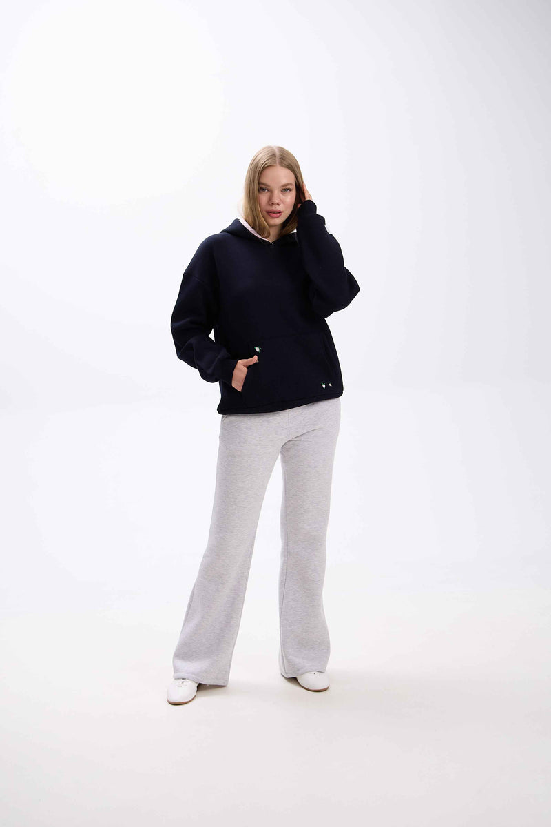 Person wearing a black hoodie and gray pants on a white background.