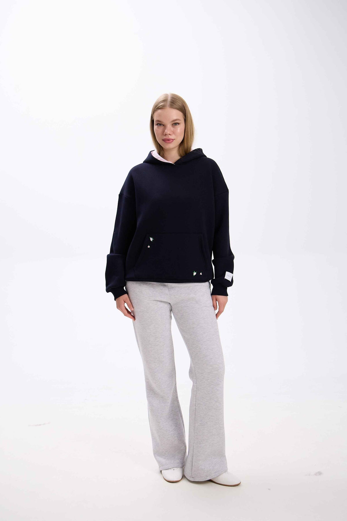 Person wearing a black hoodie and gray pants on a white background.