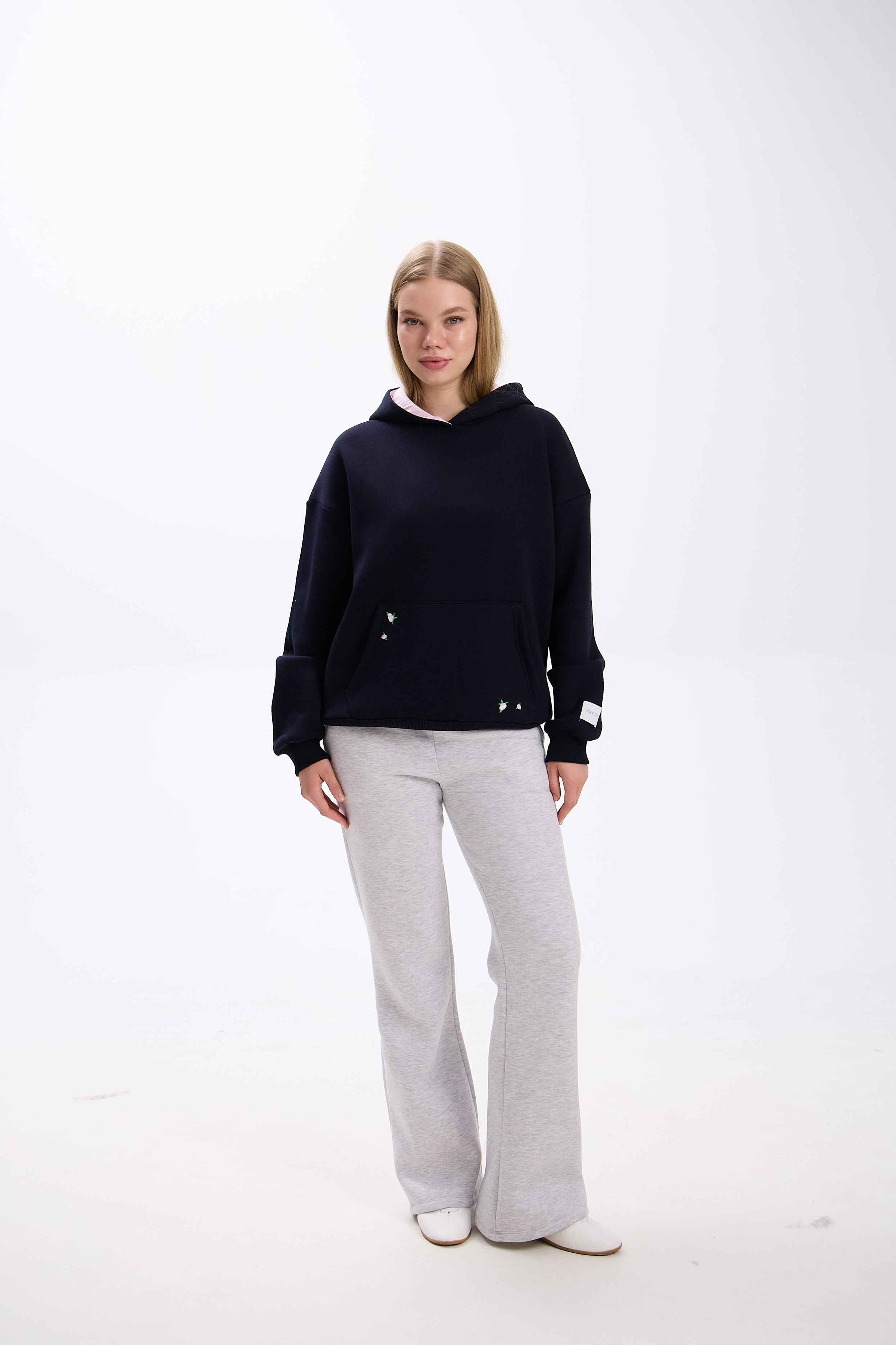 Person wearing a black hoodie and gray pants on a white background.