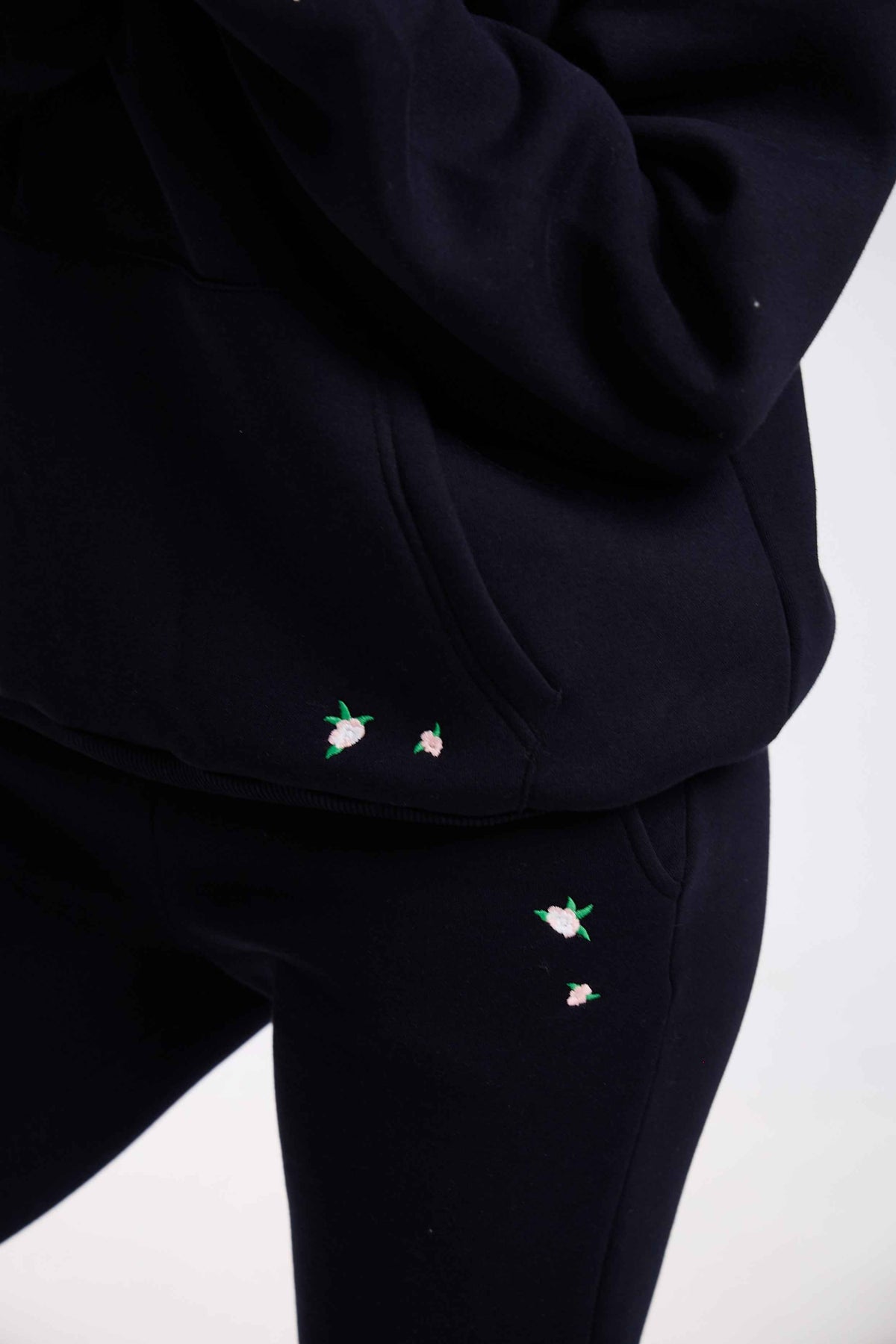 Black hoodie and pants with small embroidered designs on a white background.
