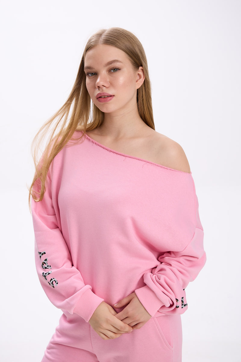 Model wearing a pink off-shoulder sweatshirt with sleeve logo detail, paired with matching sweatpants.