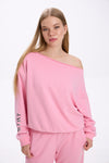 Model in a pink off-shoulder sweatshirt with logo detail on the sleeve, paired with matching pink sweatpants.