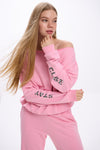 Model in a pink off-shoulder sweatshirt with “Stay Close” logo on sleeves, paired with matching sweatpants.