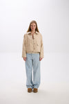 Person wearing a beige jacket and light blue jeans on a white background.