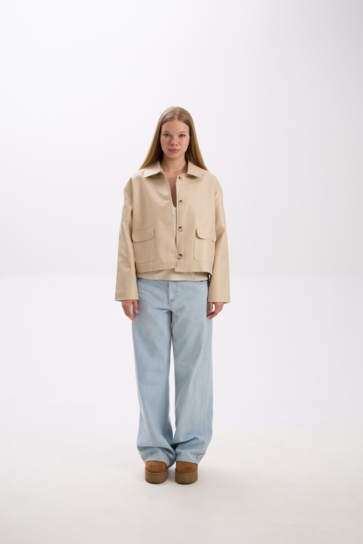 Person wearing a beige jacket and light blue jeans on a white background.