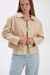 Woman wearing a beige jacket and light blue jeans on a white background.