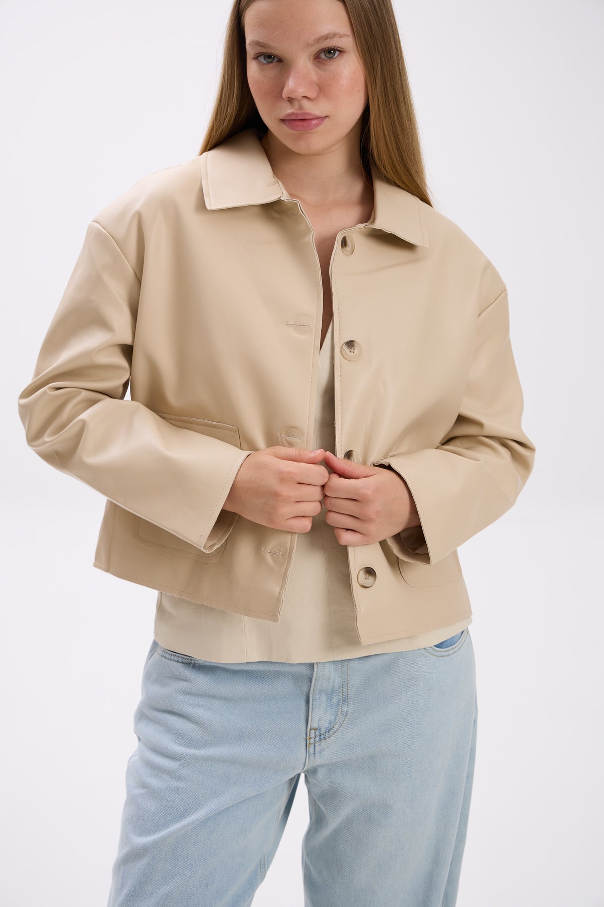 Woman wearing a beige jacket and light blue jeans on a white background.